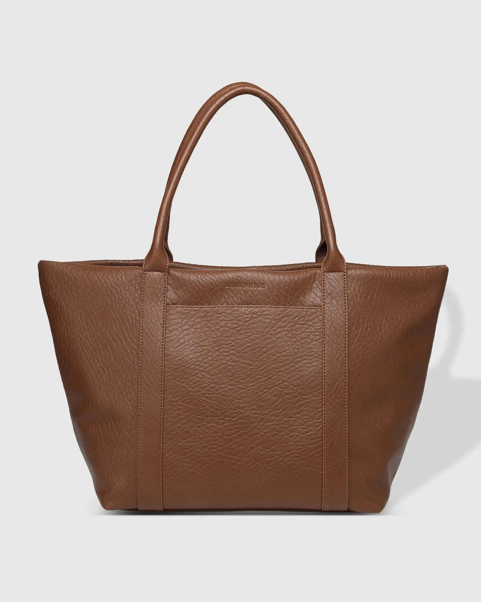 A person in white clothing stands on a porch holding The Savannah Tote Bag by Louenhide, crafted from vegan leather, resting it atop a black rolling suitcase.