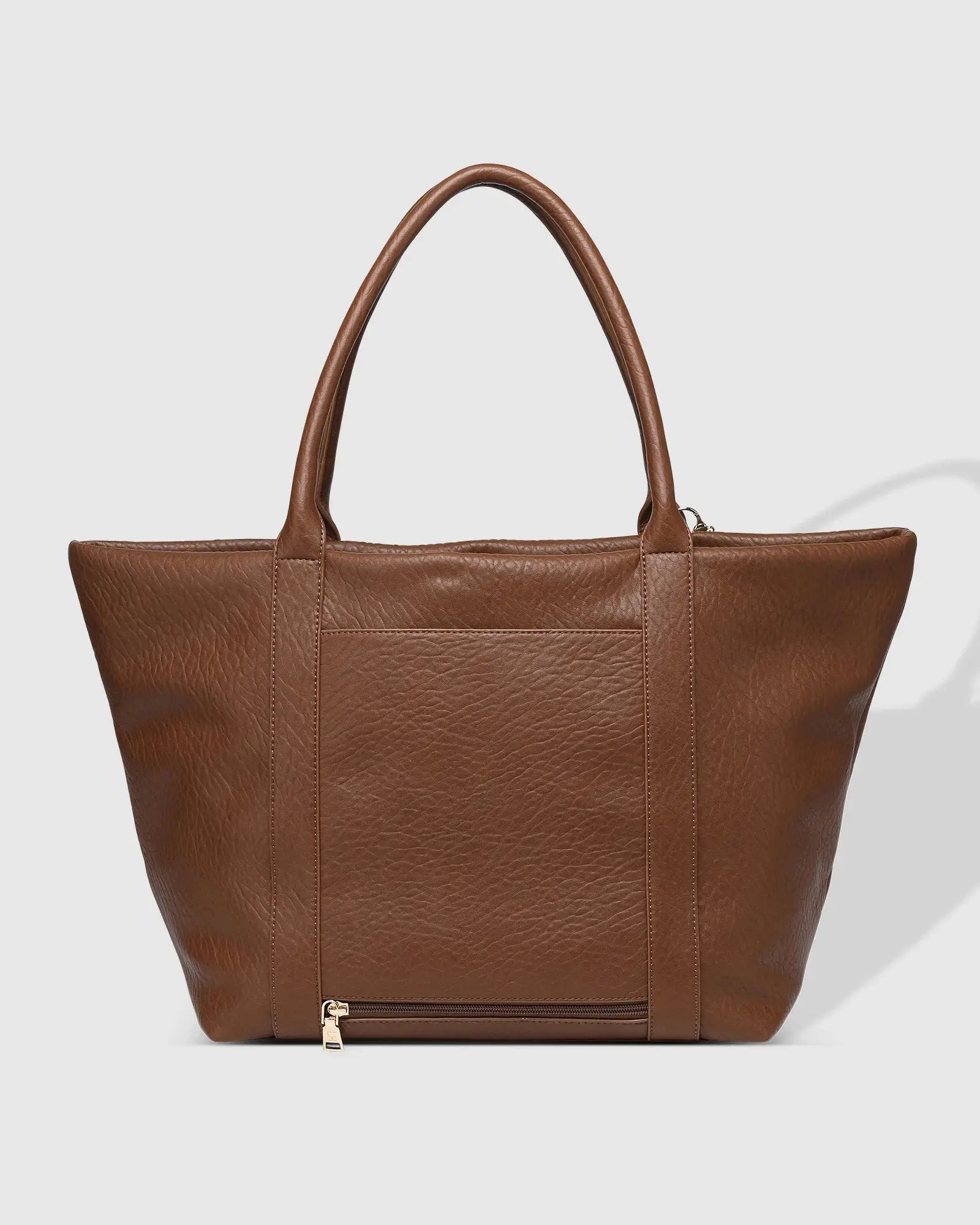 A person in white clothing stands on a porch holding The Savannah Tote Bag by Louenhide, crafted from vegan leather, resting it atop a black rolling suitcase.