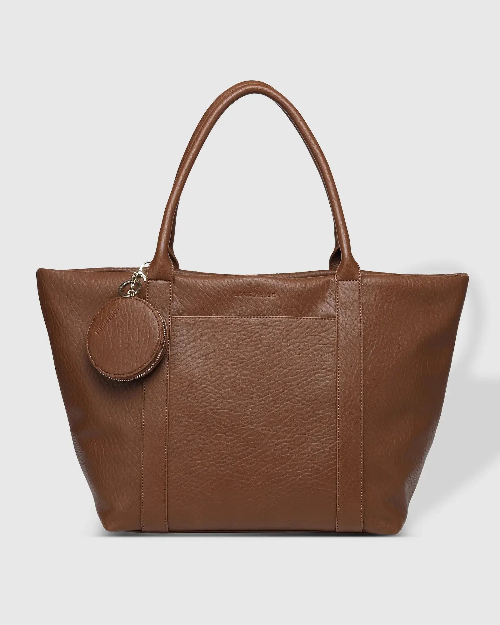 A person in white clothing stands on a porch holding The Savannah Tote Bag by Louenhide, crafted from vegan leather, resting it atop a black rolling suitcase.