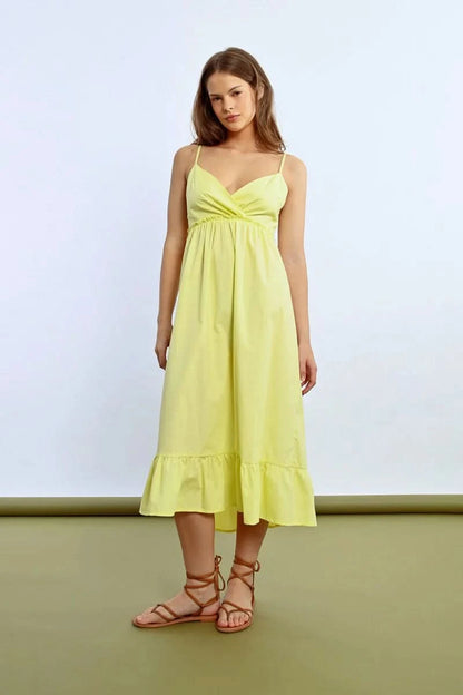 The person wears a Molly Bracken Ruffled Long Dress featuring a sleeveless design, crossed sweetheart neckline, and bow detail at the back, showing tattoos while posing sideways against a plain backdrop.