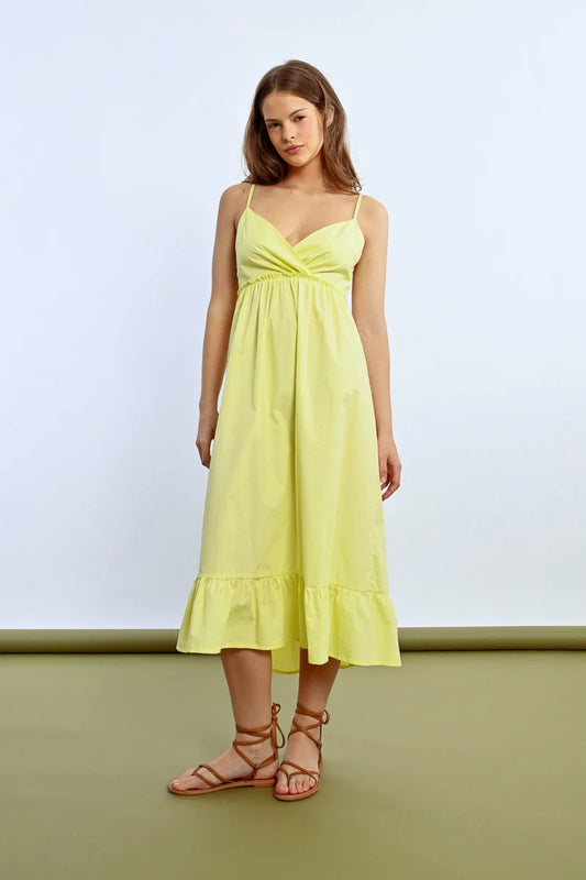 The person wears a Molly Bracken Ruffled Long Dress featuring a sleeveless design, crossed sweetheart neckline, and bow detail at the back, showing tattoos while posing sideways against a plain backdrop.