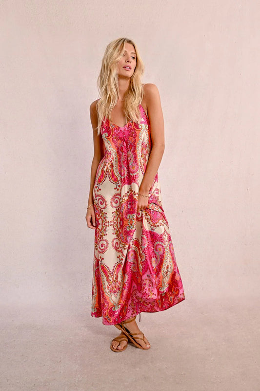 Against a plain light background, an elegant person with long hair is seen wearing a Satin Dress With Straps by Molly Bracken, along with brown sandals.