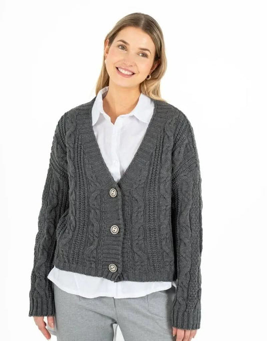 A person smiling, exuding comfort and style, is wearing a dark gray Knitted Cardigan by M Made In Italy over a white shirt and light gray pants, standing against a crisp white background.