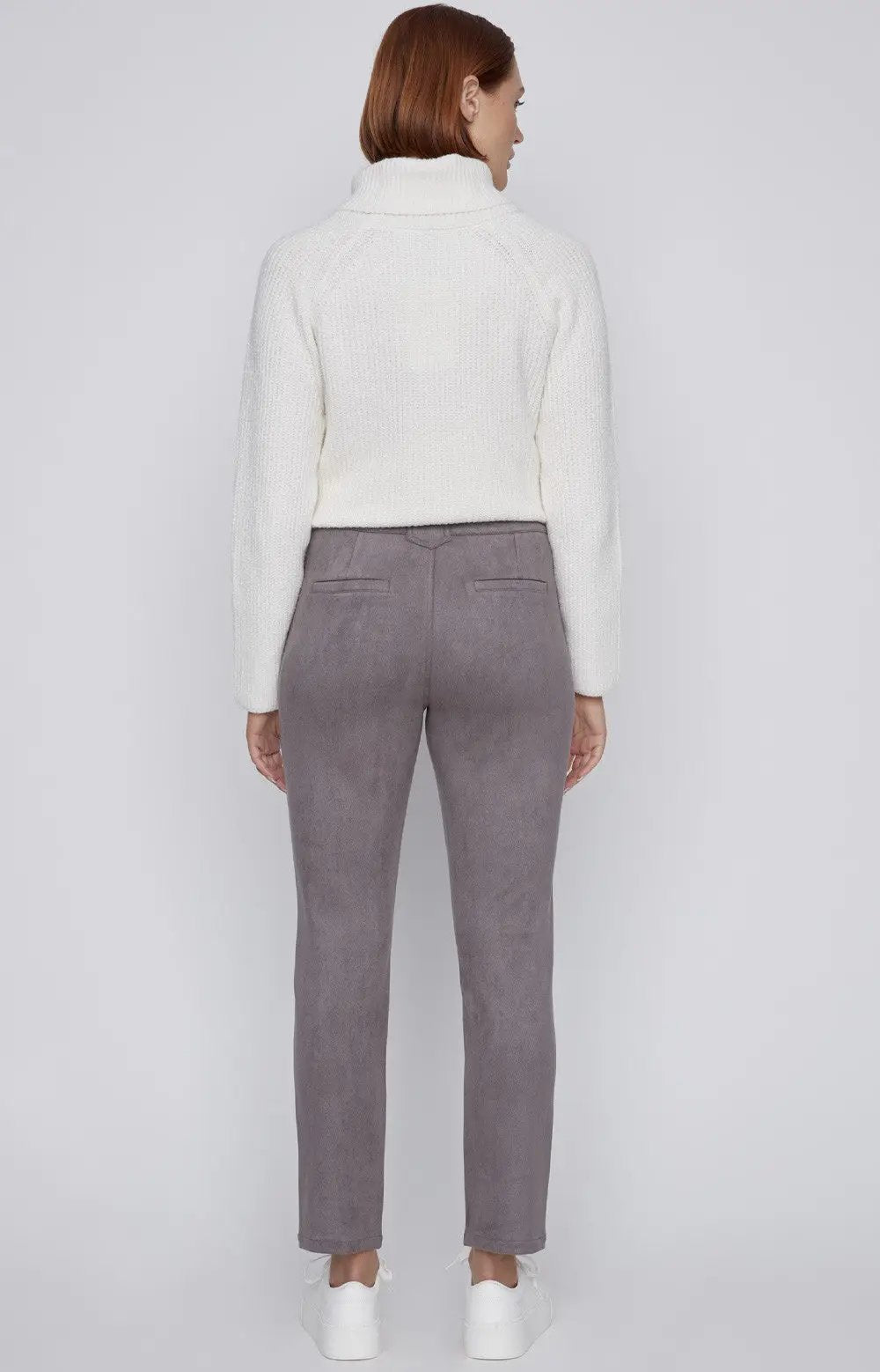 A person with short red hair is standing against a plain background, wearing a white turtleneck sweater, CoCo Y Club gray Front Zip Detail Pant, and white sneakers.