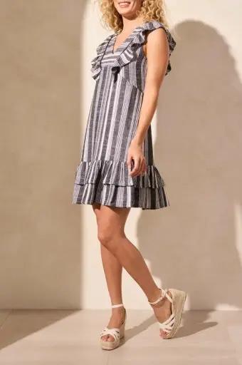 A woman wears the Tribal DRESS W/ FRILL AND TRIMS-BLACK—sleeveless with black and white stripes, frilled neckline and hem—paired with white platform sandals.
