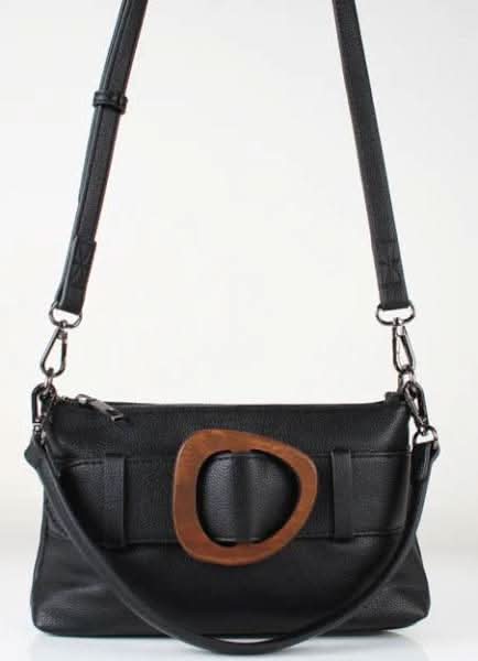 The Suma crossbody by Co-Lab is a black leather shoulder bag with an adjustable strap and a large oval brown buckle detail on the front.