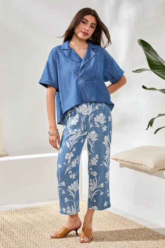 A person wearing a blue short-sleeve shirt, Tribal Flowy Wide Crop Pant, and tan heeled sandals stands indoors on a woven rug.