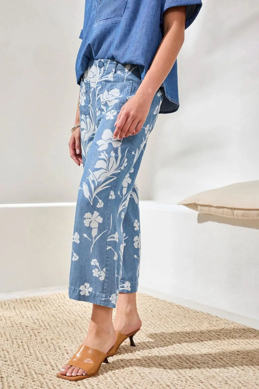 A person wearing a blue short-sleeve shirt, Tribal Flowy Wide Crop Pant, and tan heeled sandals stands indoors on a woven rug.