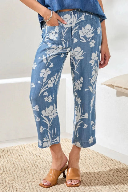 A person wearing a blue short-sleeve shirt, Tribal Flowy Wide Crop Pant, and tan heeled sandals stands indoors on a woven rug.