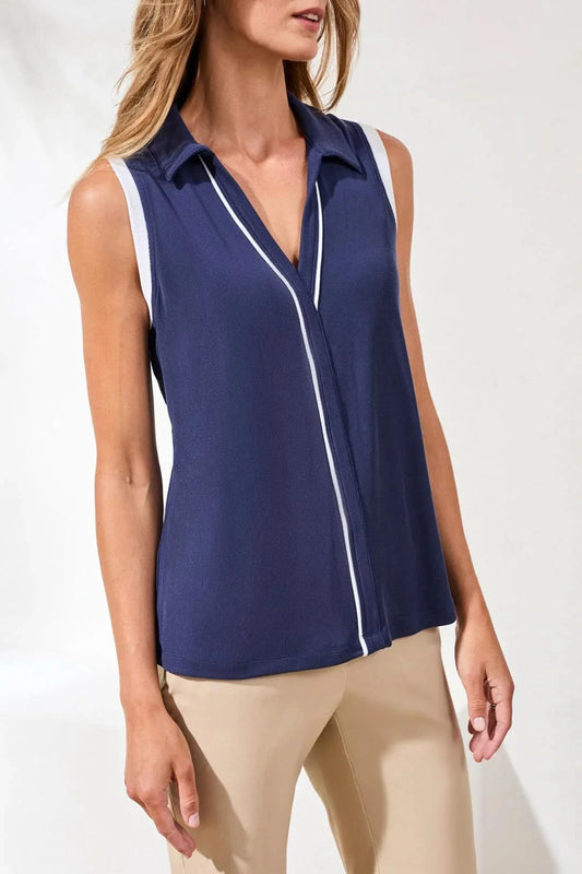 A woman stands indoors against a plain background wearing the Tribal SLEEVELESS JOHNNY COLLAR TOP in green with white trim, paired with a matching green skirt.