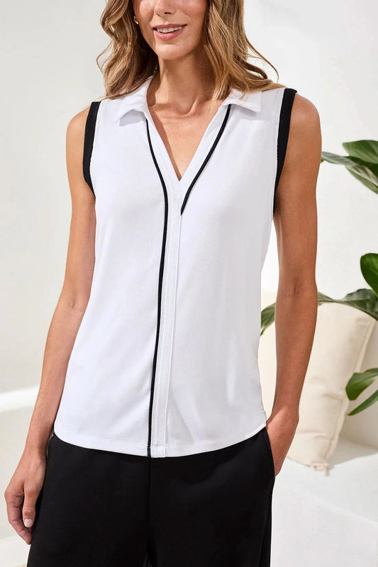 A woman stands indoors wearing the Tribal JOHNNY COLLAR MODAL TOP with black trim and loose black pants. One hand is in her pocket as she smiles slightly; a plant and cushions in the background complete this effortless summer look.