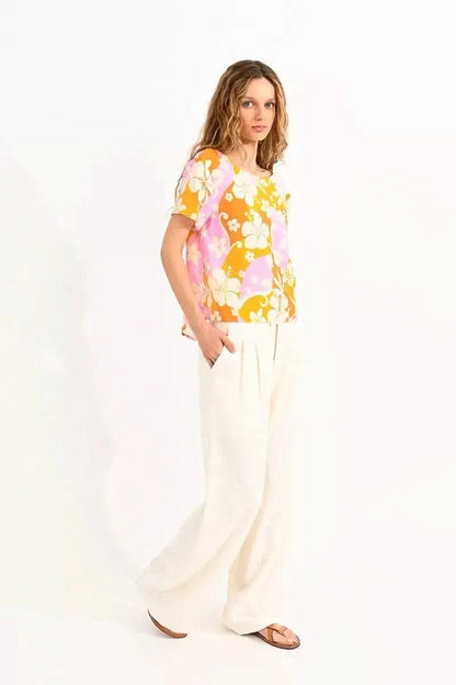 Woman in a floral orange Molly Bracken twisted back top and white pants posing against a neutral background.
