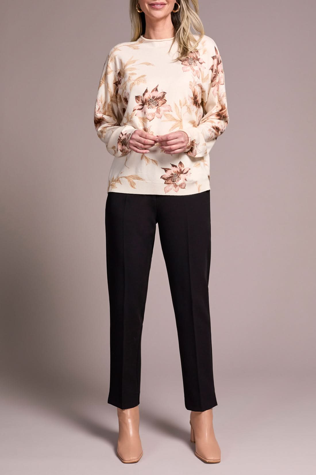 A woman models the Tribal FUNNEL NECK SWEATER with a floral print, paired with black pants and beige heels, posed against a plain neutral background.
