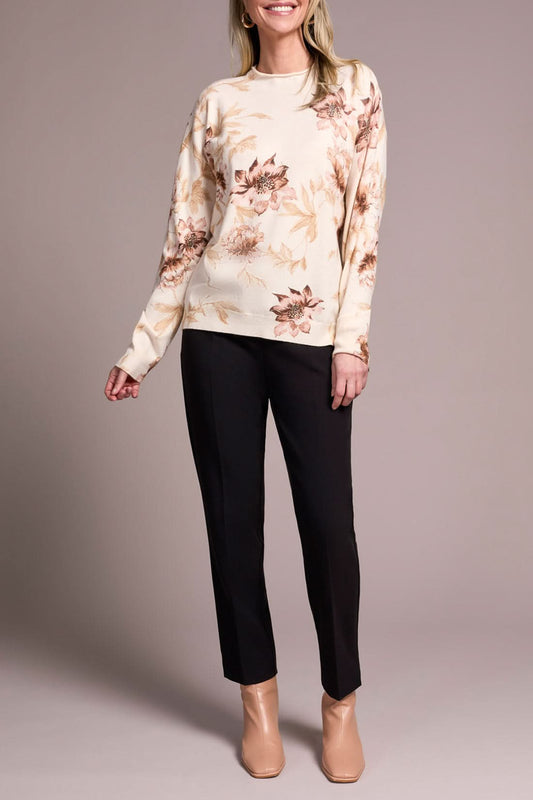 A woman models the Tribal FUNNEL NECK SWEATER with a floral print, paired with black pants and beige heels, posed against a plain neutral background.