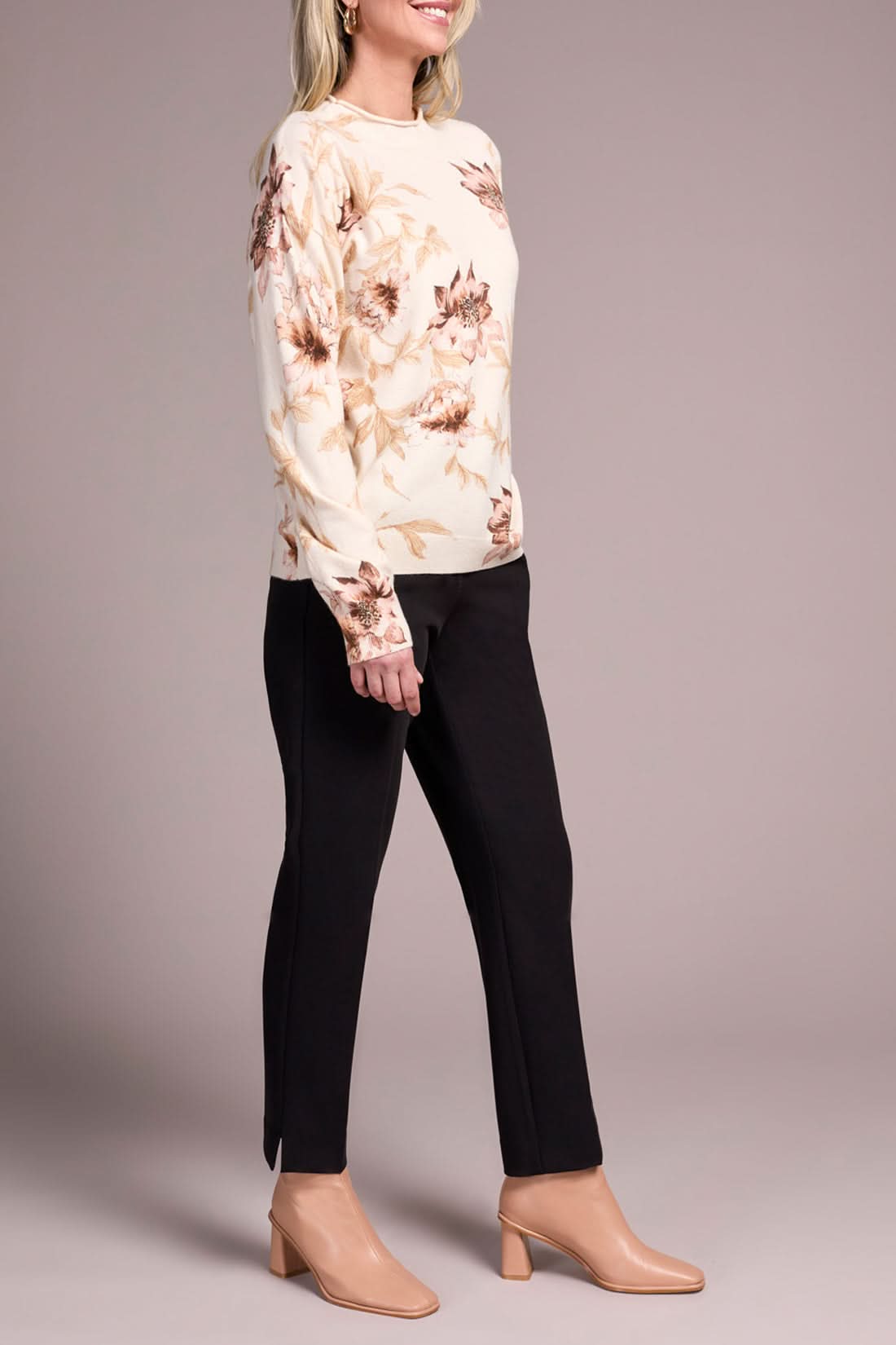 A woman models the Tribal FUNNEL NECK SWEATER with a floral print, paired with black pants and beige heels, posed against a plain neutral background.