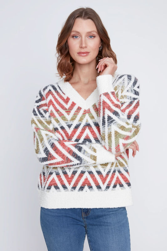 A woman in a CoCo Y Club V neck knitted Sweater with a multicolored zigzag pattern stands with one arm crossed, the other touching her chin, and pairs the cozy piece with blue jeans.
