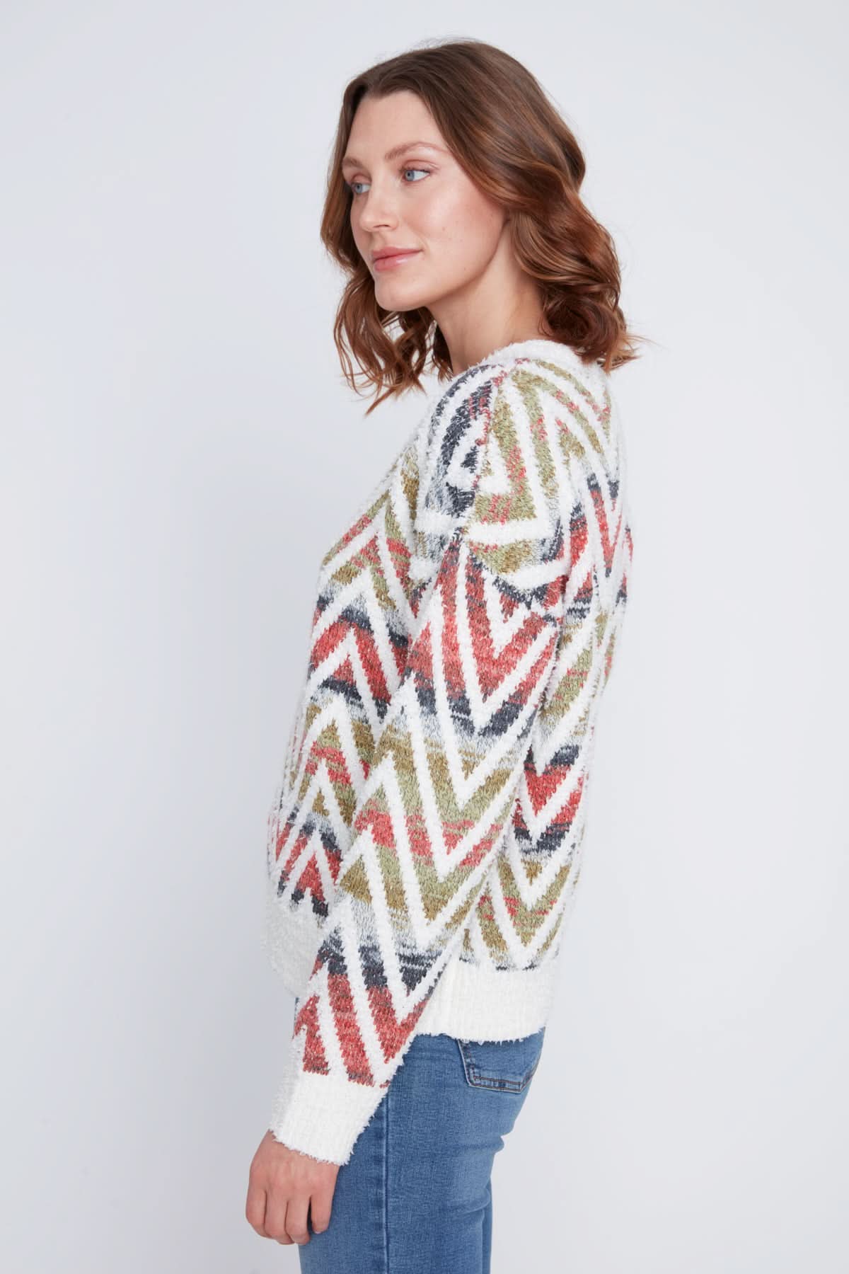 A woman in a CoCo Y Club V neck knitted Sweater with a multicolored zigzag pattern stands with one arm crossed, the other touching her chin, and pairs the cozy piece with blue jeans.