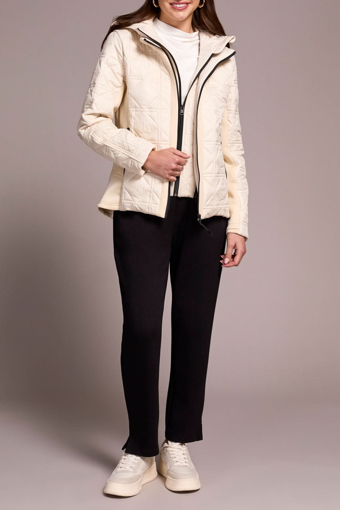 A person wears the Tribal Puffer W/Removable Hood in cream, paired with a white turtleneck, black pants, and white sneakers, standing against a plain background.