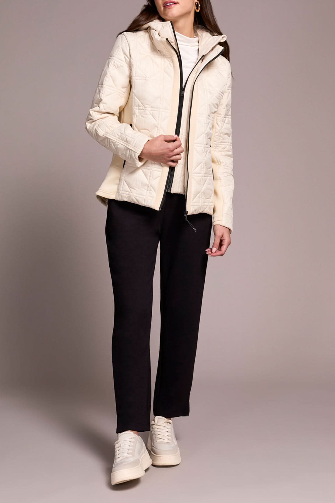 A person wears the Tribal Puffer W/Removable Hood in cream, paired with a white turtleneck, black pants, and white sneakers, standing against a plain background.