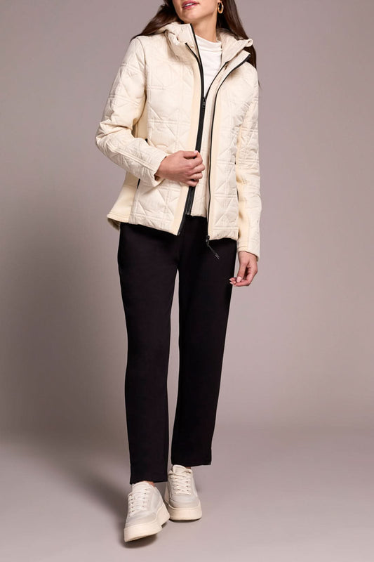 A person wears the Tribal Puffer W/Removable Hood in cream, paired with a white turtleneck, black pants, and white sneakers, standing against a plain background.
