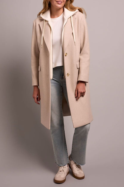 A person models the Tribal TRENCH COAT W/HOODIE, paired with light blue jeans and white sneakers, against a plain background.