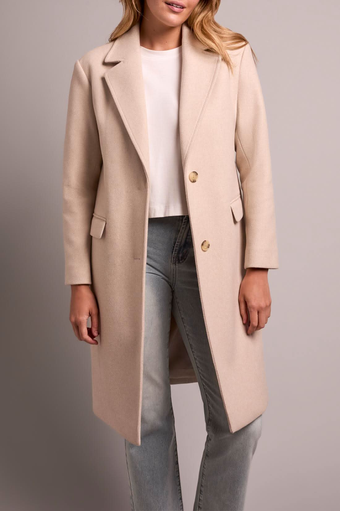 A person models the Tribal TRENCH COAT W/HOODIE, paired with light blue jeans and white sneakers, against a plain background.