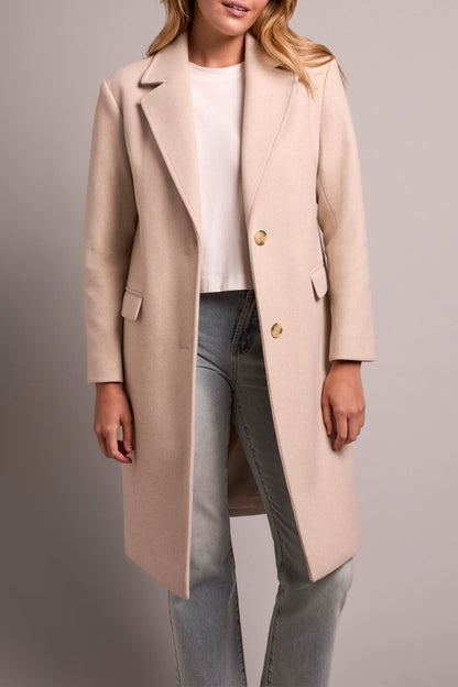 A person models the Tribal TRENCH COAT W/HOODIE, paired with light blue jeans and white sneakers, against a plain background.