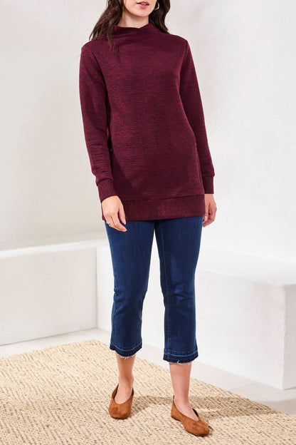 A person wears the Tribal TUNIC W/POCKETS in wine, blue cropped jeans, and brown flats while standing indoors on a woven rug.