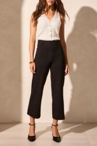 A person wears Tribal's High Rise Capri, black wide-leg cropped pants with front pockets, styled with a sleeveless white top and black heels.