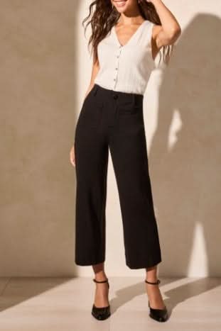 A person wears Tribal's High Rise Capri, black wide-leg cropped pants with front pockets, styled with a sleeveless white top and black heels.