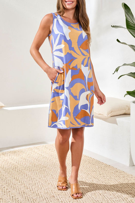 A woman stands indoors on a woven rug by a plant, wearing the Tribal Short Sleeve Summer Dress featuring a blue, white, and orange abstract print.