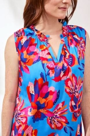 A woman wears the Tribal CHALLIS FRILL BLOUSE—a sleeveless blue top with a vibrant multicolored floral print, notched neckline, and comfy stretch challis fabric.
