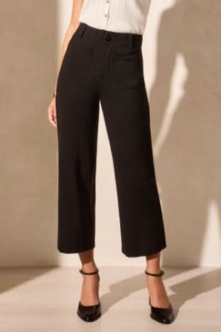 A person wears Tribal's High Rise Capri, black wide-leg cropped pants with front pockets, styled with a sleeveless white top and black heels.
