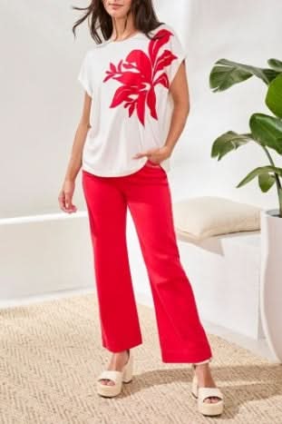 A woman wearing the Tribal CAP SLEEVE TOP in ultra-soft jersey with a large red floral patch on the front, paired with red pants.