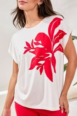A woman wearing the Tribal CAP SLEEVE TOP in ultra-soft jersey with a large red floral patch on the front, paired with red pants.