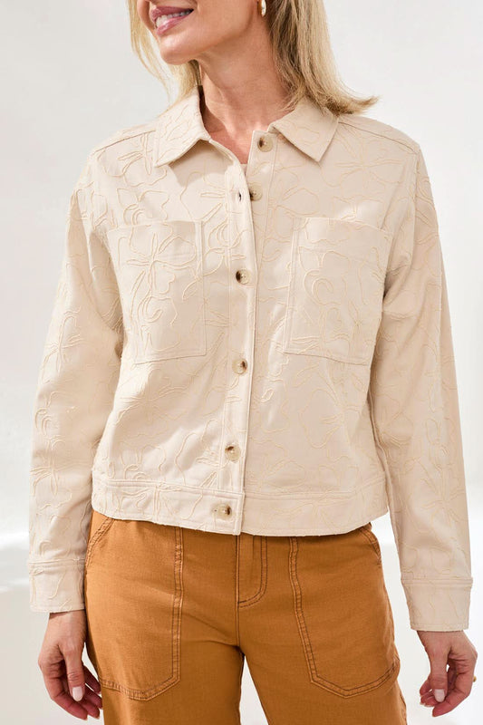 A woman wears the Tribal Floral Textured Jacket, a light beige, long-sleeve button-front piece with front pockets and floral embroidery, styled with high-waisted brown pants.