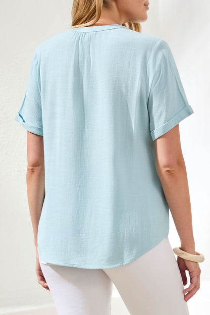 A woman wears the Tribal Chic Coastal Shirt—a light blue, short sleeve linen-rayon blouse with buttons—shown from shoulders to mid-torso against a white background.