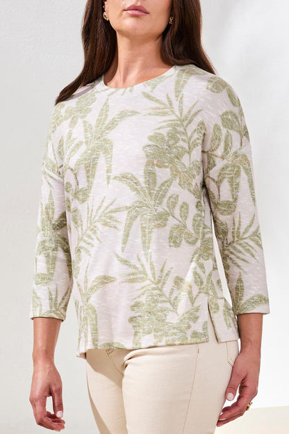 A woman models the Tribal 3/4 sleeve Crew Neck Top with a green leaf print, paired with beige pants, against a plain white background.
