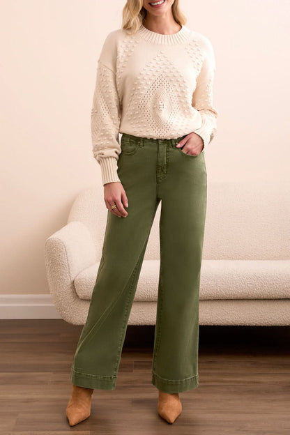 A woman stands indoors in Tribal FLY FRONT WIDE LEG PANTS, a cream knit sweater, and tan heels, posed by a light sofa on a wooden floor.