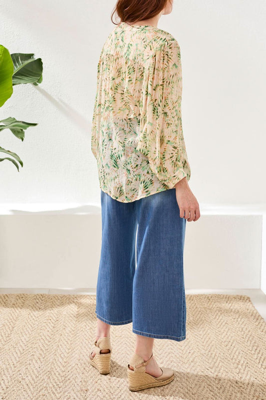 A woman wears the Tribal Dolman Sleeve Blouse, paired with wide-leg blue jeans and beige wedge sandals, standing on a woven rug against a white background.
