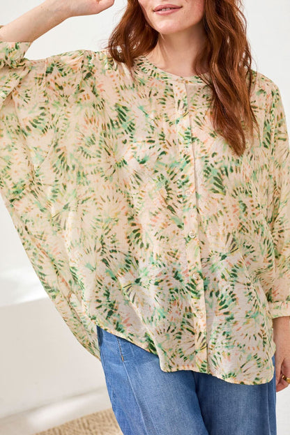 A woman wears the Tribal Dolman Sleeve Blouse, paired with wide-leg blue jeans and beige wedge sandals, standing on a woven rug against a white background.