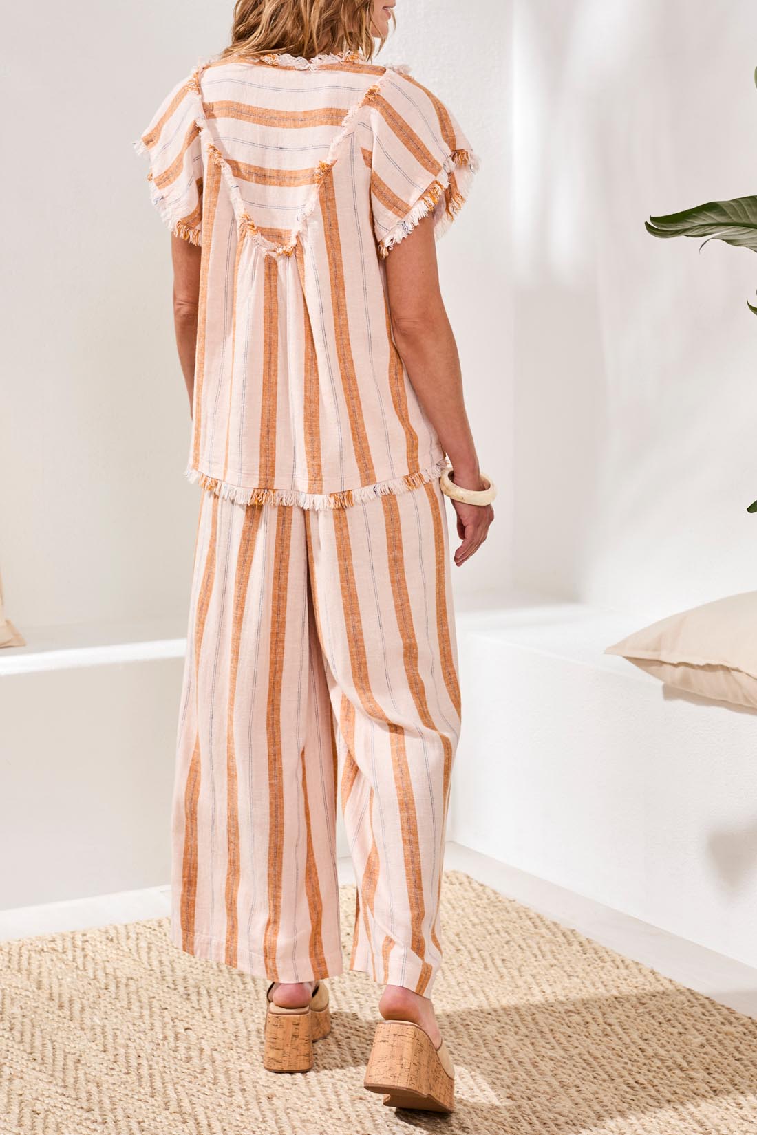 A woman with shoulder-length dark hair stands outdoors, smiling at the camera under a blue sky while wearing the Tribal Cap Sleeve T-Blouse.