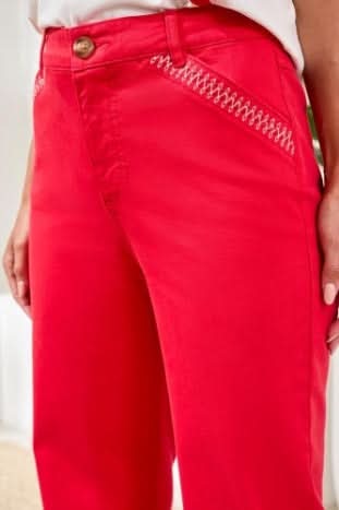 A person wearing Tribal’s Fly Front Ankle Pant with embroidery detail, featuring bright pink fabric, white zigzag stitching near the pockets, and a brown waistband button.