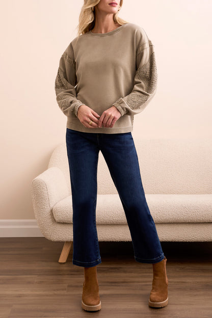A woman stands indoors wearing the Tribal CREW NECK APPLIQUE DTL sweater, blue cropped jeans, and brown suede ankle boots, with a cream sofa in the background.