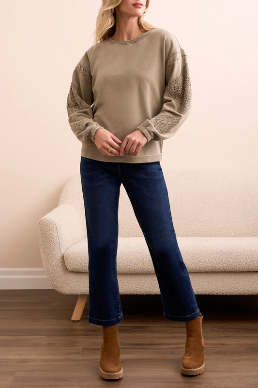 A woman stands indoors wearing the Tribal CREW NECK APPLIQUE DTL sweater, blue cropped jeans, and brown suede ankle boots, with a cream sofa in the background.