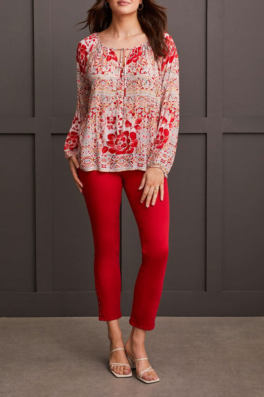 A person wearing a Tribal Blouse with Tie, featuring a red and white pattern, paired with red pants, stands against a gray background.