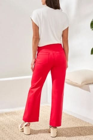 A person wearing Tribal’s Fly Front Ankle Pant with embroidery detail, featuring bright pink fabric, white zigzag stitching near the pockets, and a brown waistband button.