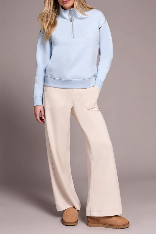 A person models the Tribal ZIP FUNNEL NECK TOP in light blue, paired with beige wide-leg pants and tan suede slippers, standing against a plain background.