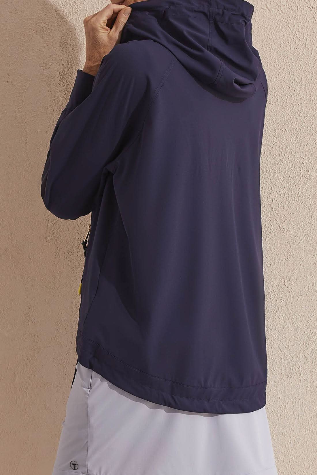 A person wearing a Tribal navy blue hooded sport golf jacket with yellow zipper detail and a white shirt underneath.