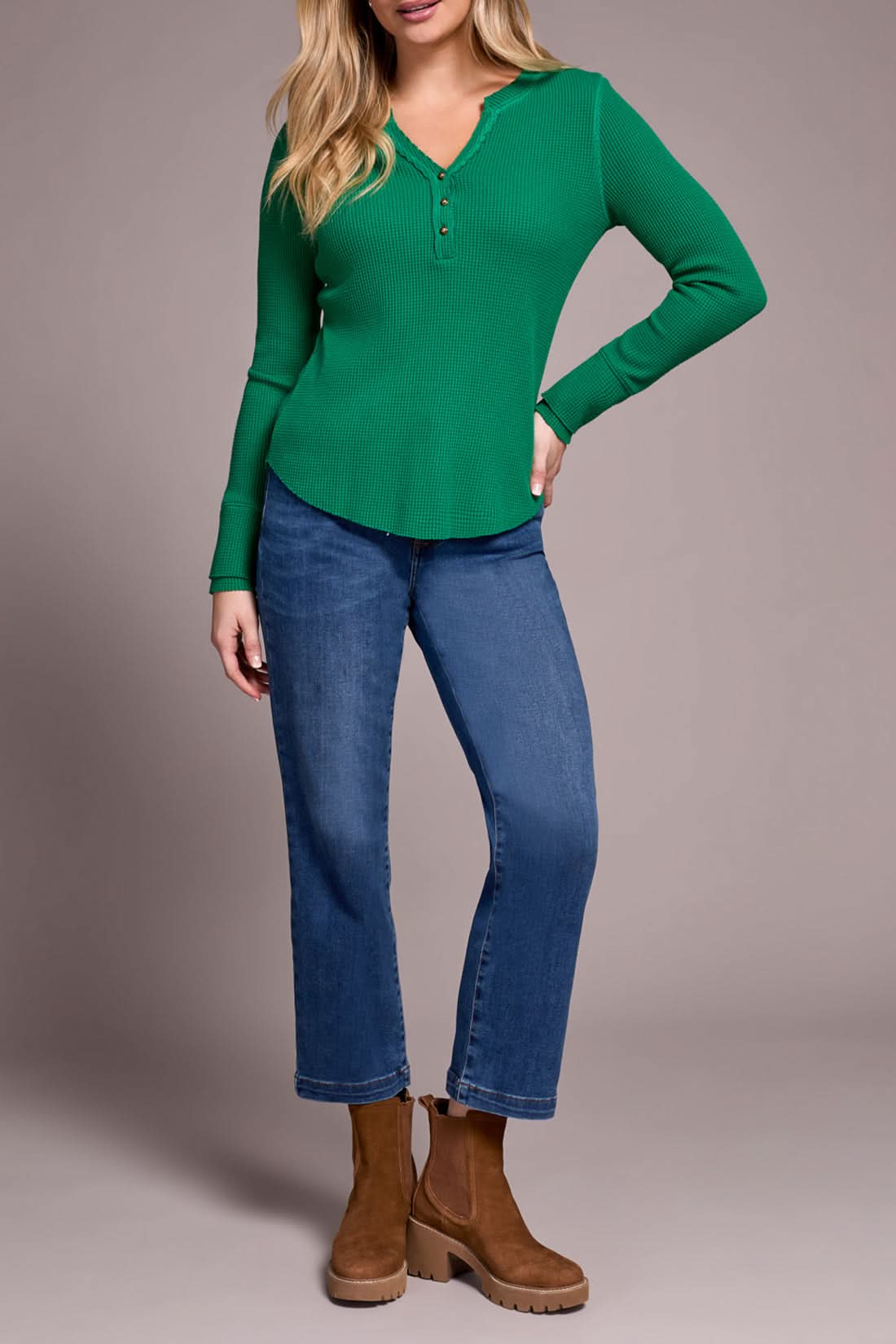 A woman indoors wears the Tribal HENLEY TOP in light blue with matching pants and beige ankle boots, standing by a cream sofa and a plant, embodying a chic, versatile style.